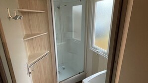 A small, compact bathroom with a glass shower enclosure, a toilet, and a sink. - 3-bedroom mobile home with pool (Camiers)