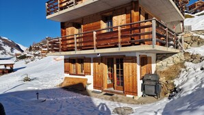 A wooden chalet with a balcony, stone walls, and a snow-covered landscape.
