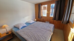 A small, cozy room with a single bed, a bedside table with a lamp, and a window with curtains.