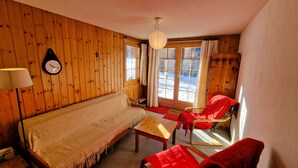 A cozy room with a wooden interior, a sofa, a red chair, a small table, and a lamp.