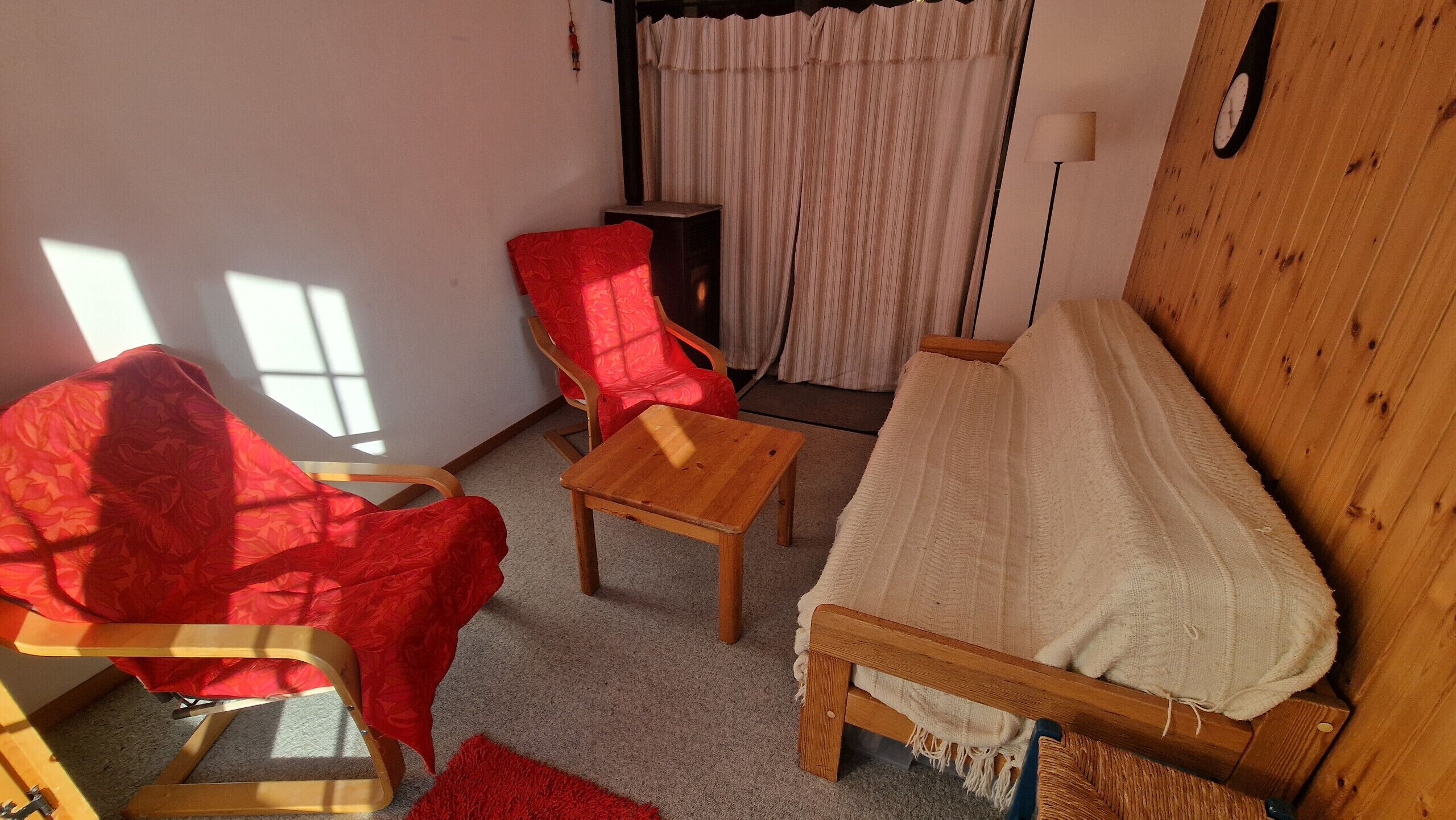 Un accogliente soggiorno con un divano in legno, una poltrona rossa, un tavolino in legno e una sedia rossa a motivi.