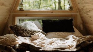 A cozy bedroom with a sloped ceiling, a window with a view of trees, a bed with a blanket, and a nightstand with a lamp. - Prunella № 3, Prunella № 3 - A-Frame Cabin Getaway - Design, Comfort & Nature (Thorne)