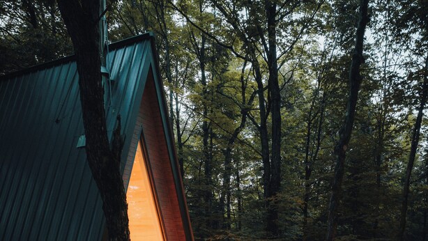 Ein Baumhaus mit Glasfront, Holzboden und Sitzbereich im Freien.