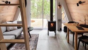 Ein gemütlicher Dachbodenraum mit Holzvertäfelung, einem Kamin, einem Schlafplatz in der Schräge und Blick ins Freie.