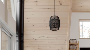 A modern living room with a large black wood-burning stove, a wooden ceiling, a grey sofa, and a hanging light fixture. - Prunella № 1, Prunella № 1 - A-Frame Cabin Getaway - Design, Comfort & Nature (Thorne)