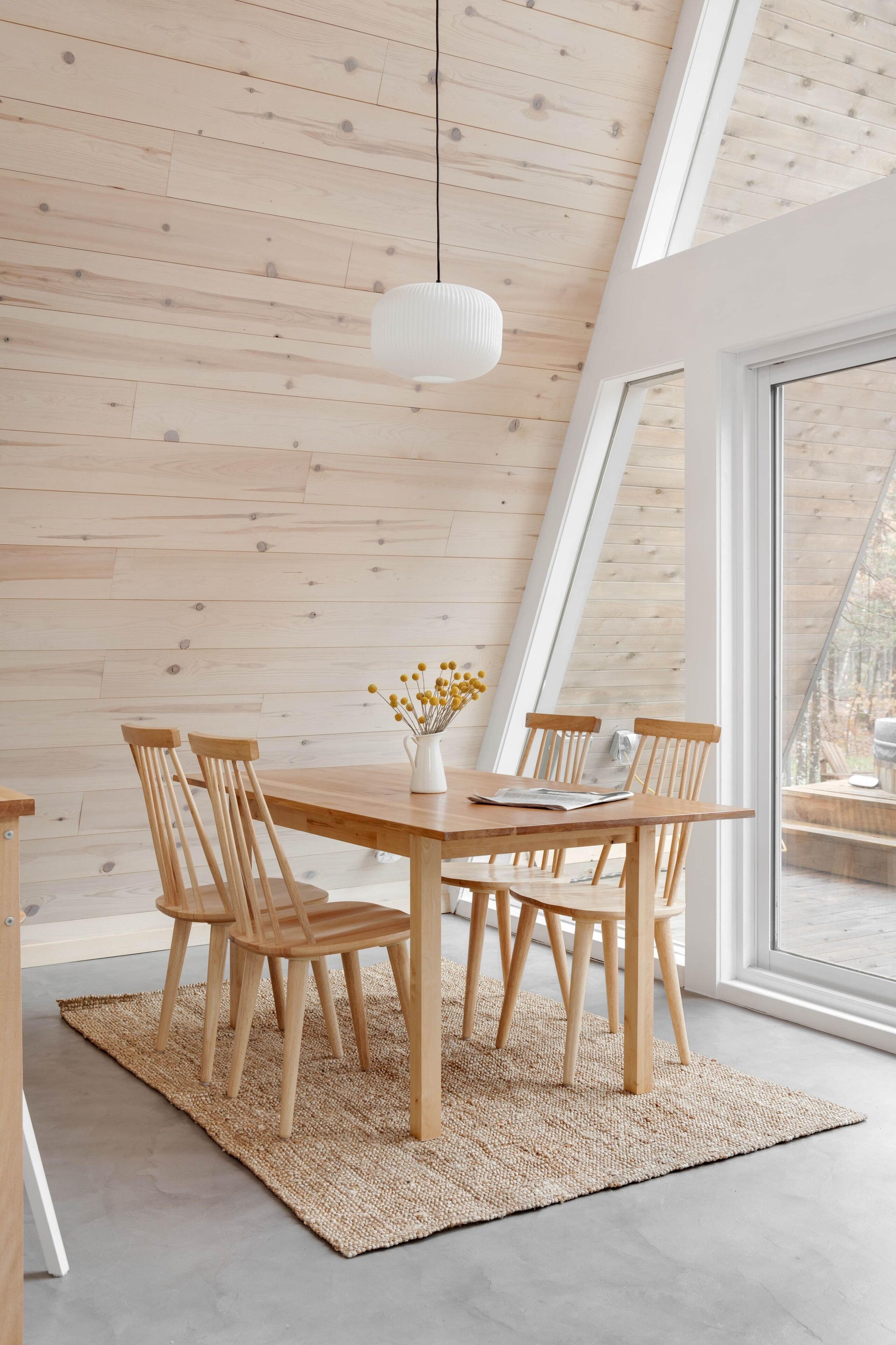 Ein Essbereich mit einem Holztisch und Stühlen, einem gewebten Teppich und einer hängenden Leuchte.