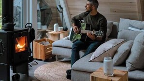 A cozy living room with a wood-burning stove, a sofa, and a person playing a guitar. - Prunella № 1, Prunella № 1 - A-Frame Cabin Getaway - Design, Comfort & Nature (Thorne)