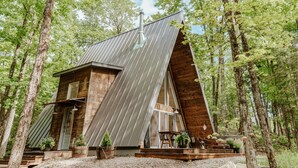A modern cabin with a sloped roof, wooden exterior, and a small porch with seating. - Prunella № 1, Prunella № 1 - A-Frame Cabin Getaway - Design, Comfort & Nature (Thorne)