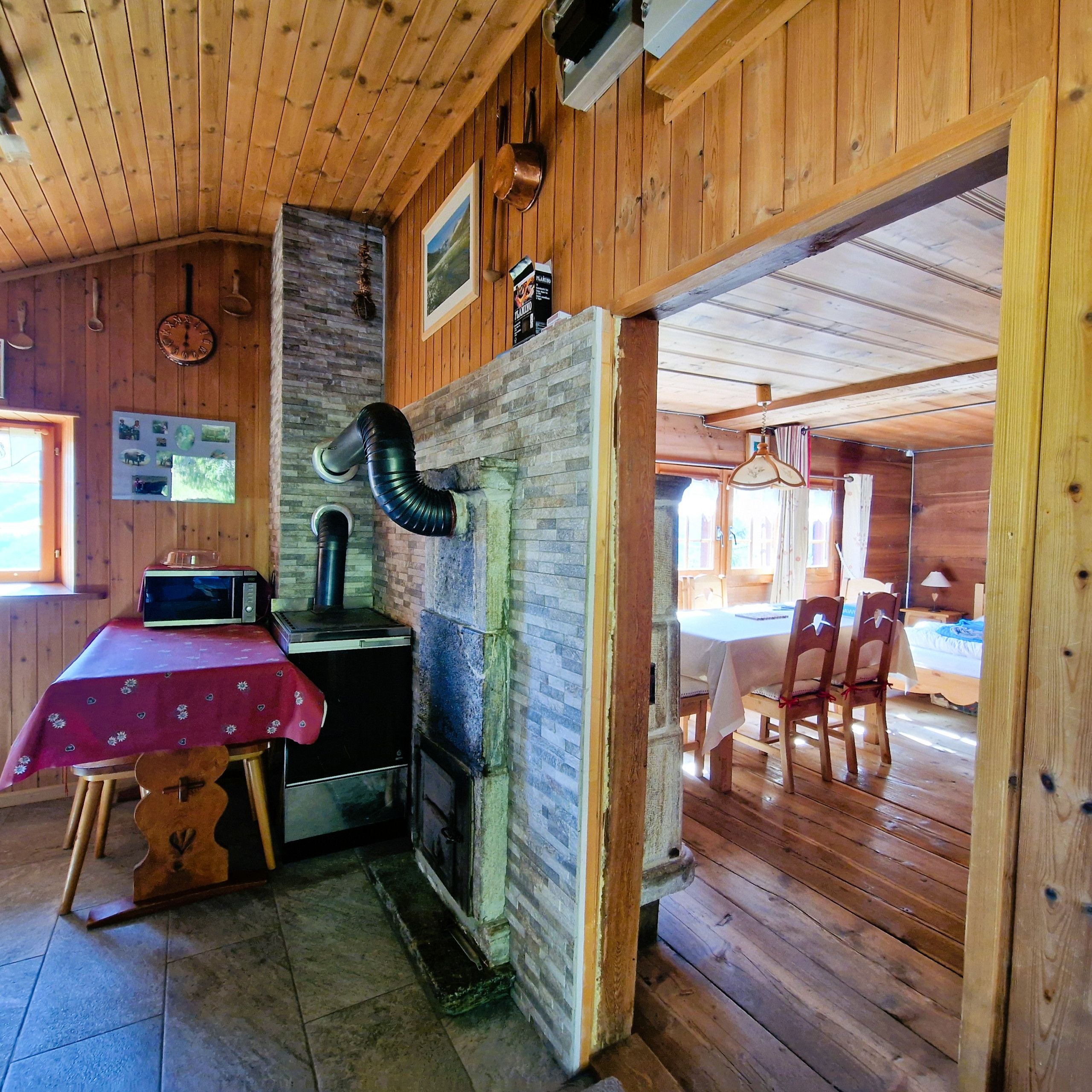 A rustic wooden interior with a kitchen area featuring a stove, microwave, and a table with a red tablecloth.