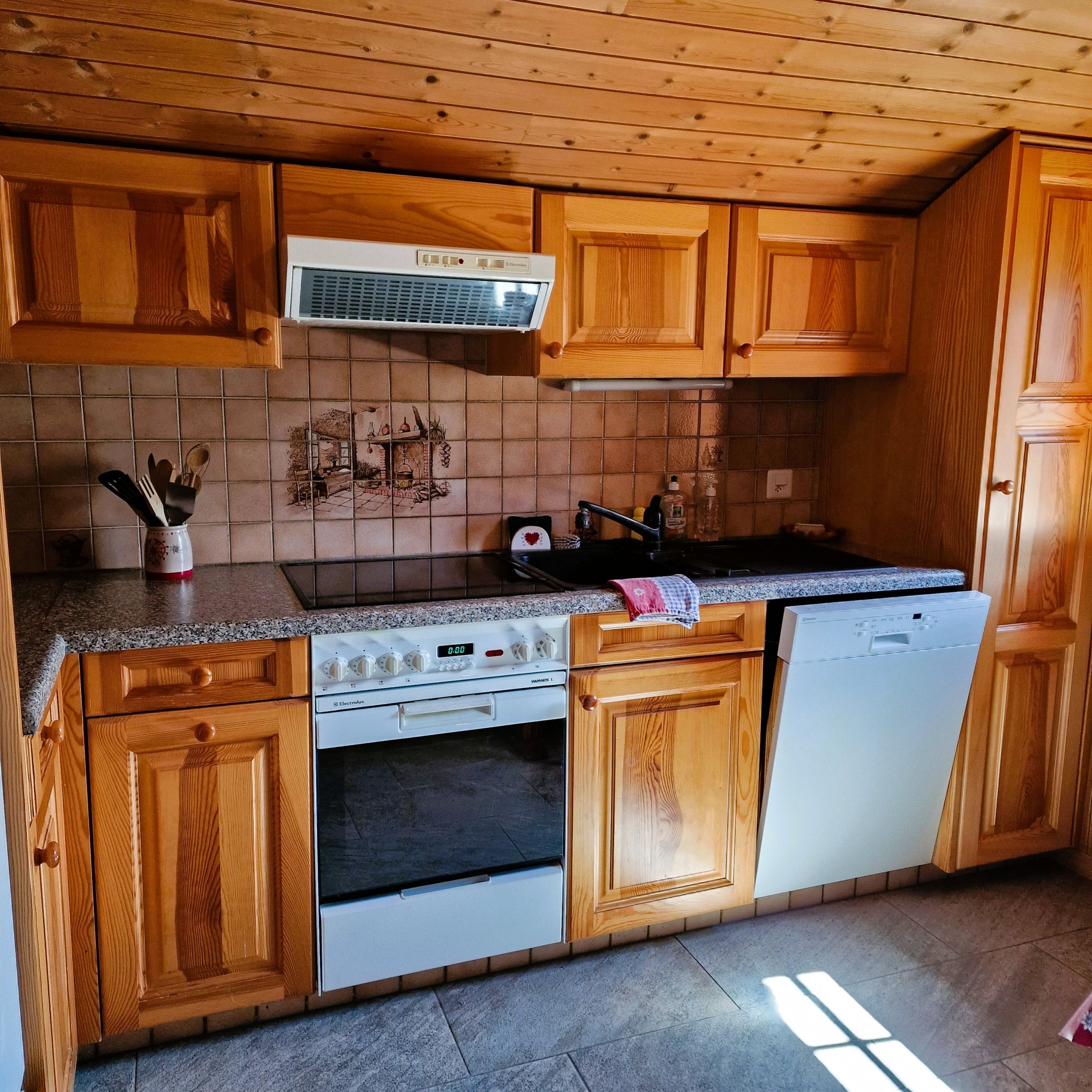 Une cuisine avec des meubles de rangement en bois, une cuisinière, un lave-vaisselle et un dosseret carrelé.