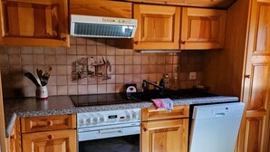 Une cuisine avec des meubles de rangement en bois, une cuisinière, un lave-vaisselle et un dosseret carrelé.