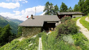 Une maison en pierre avec un toit en pente, une antenne parabolique et une petite dépendance attenante dotée d’une porte.