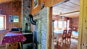 A rustic wooden interior with a kitchen area featuring a stove, microwave, and a table with a red tablecloth. - Mayen Motau - Retour à l'essentiel | La Forclaz (La Forclaz)