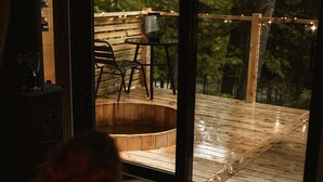 Un dormitorio con un ventanal que da a una terraza de madera con mobiliario exterior y luces colgantes.