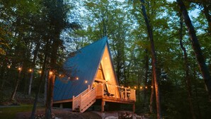 Una cabaña con techo triangular, terraza de madera y luces colgantes.
