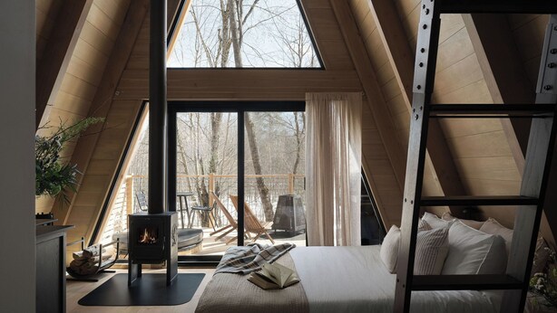 Un dormitorio acogedor en el ático con un gran ventanal, una cama de madera tipo camarote, una chimenea y una escalera.