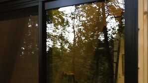 Un dormitorio con cama, almohadas y ventana con vistas a un bosque.