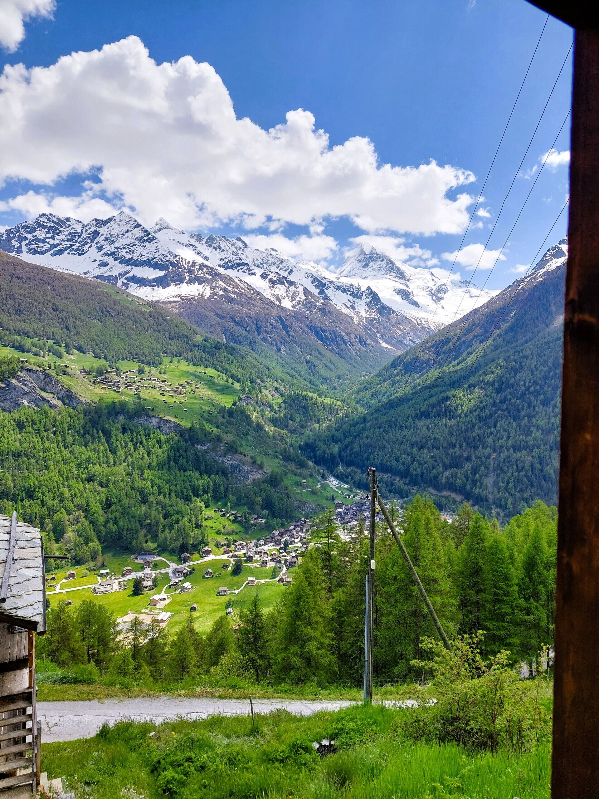 A mountainous landscape with a village nestled in a valley, surrounded by snow-capped peaks and dense forests.