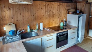 A kitchen with wooden walls, a sink, a stove, and a refrigerator. - Mayen Farquesses (Evolène)