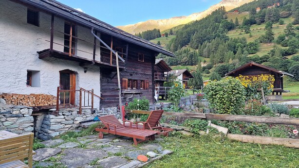 A rustic chalet with a stone foundation, wooden balconies, and a garden with a wooden bench. - Chalet Berthé 11 (Les Haudères)