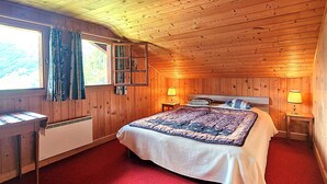 A wooden cabin bedroom with a bed, a window with curtains, a heater, and a lamp on a bedside table. - Chalet Tourbillon Gerber - La Sage (La Sage)