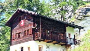 A wooden chalet with a balcony, set against a backdrop of trees and a rocky cliff. - Chalet Tourbillon Gerber - La Sage (La Sage)