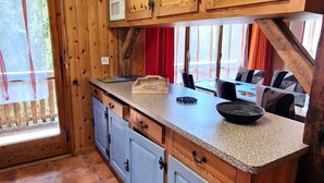 A kitchen with wooden cabinets, a countertop, and a window with a view of the outdoors. - Beau Séjour 2 (Evolène)