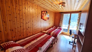 A room with wooden walls and a large window. There are two beds with red and white checkered bedding. A painting of palm trees is on the wall. - Beau Séjour 2 (Evolène)
