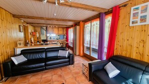A cozy wooden interior with a black leather sofa, a small table, and a kitchen area with wooden cabinets and a tiled floor. - Beau Séjour 2 (Evolène)