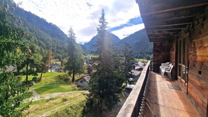 A wooden balcony with a view of a valley, houses, and mountains.