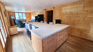 A modern kitchen with wooden cabinetry, a central island, and a dining area with chairs.