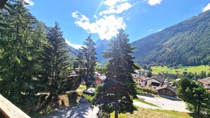 A mountain village with traditional wooden houses, a clear road, and a valley with greenery and mountains in the background.