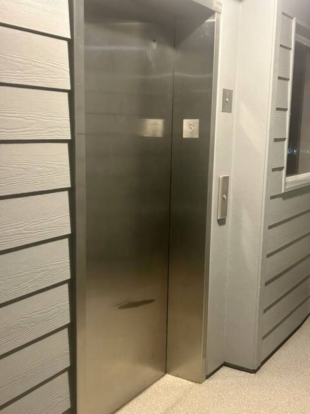 A metallic elevator door with a control panel and a number plate.