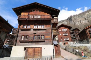 A traditional wooden chalet with multiple balconies, a satellite dish, and a mountain backdrop.