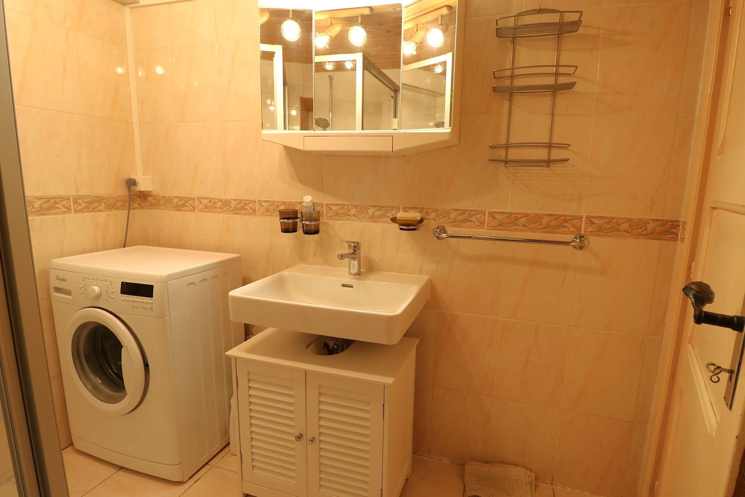 Ein kleines Badezimmer mit Waschmaschine, Waschbecken und Spiegel.