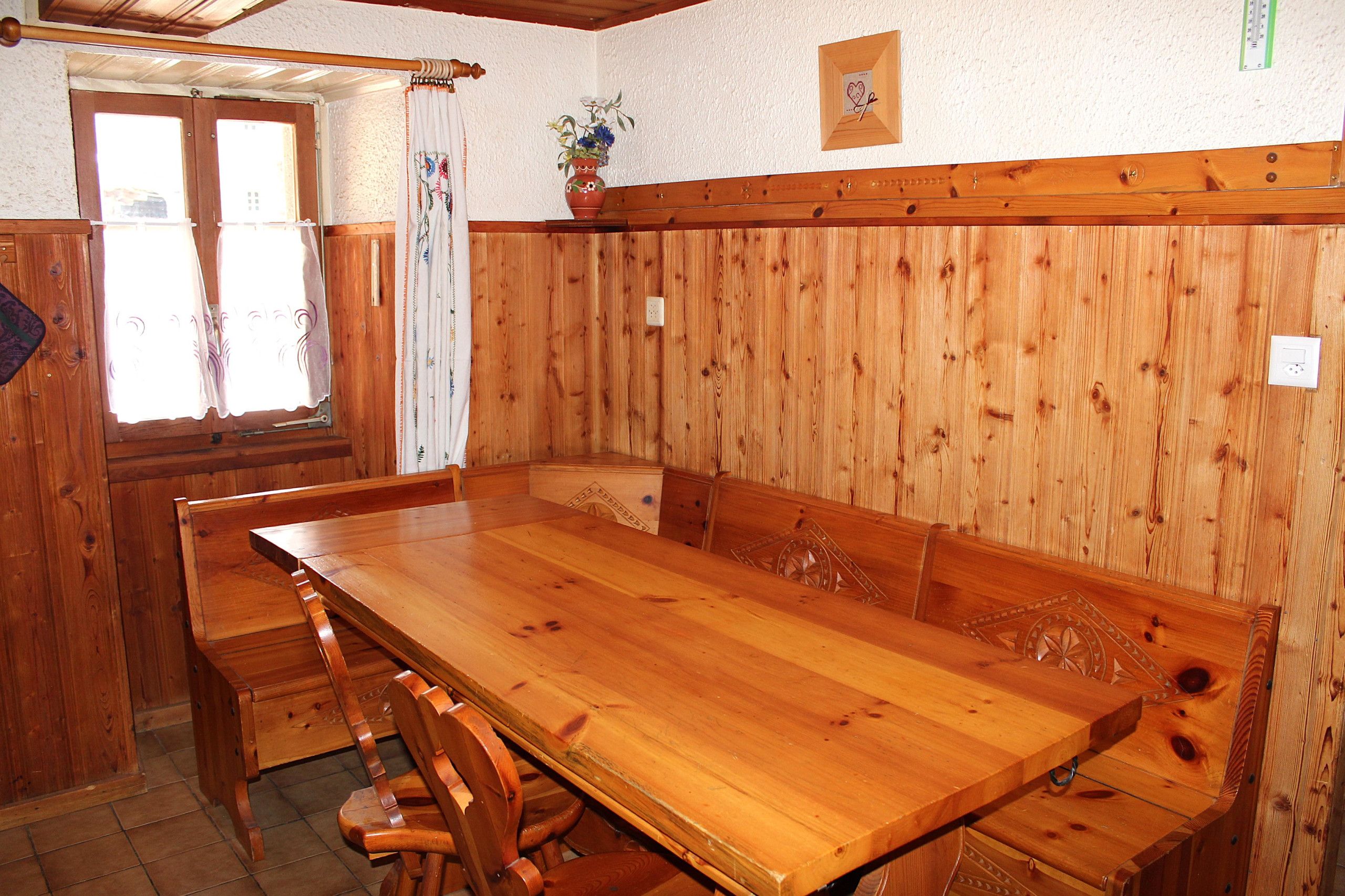 Un tavolo da pranzo in legno con panche, una finestra con tende e un vaso con fiori fissato alla parete.