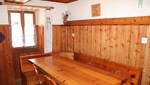 Una mesa de madera con bancos, una ventana con cortinas y un florero de pared con flores.
