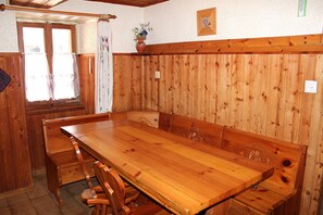 A wooden dining table with benches, a window with curtains, and a wall-mounted vase with flowers.