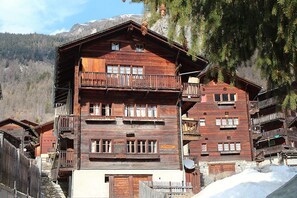 Un bâtiment en bois à plusieurs étages, doté de balcons, avec une enseigne indiquant « Le Trophée », et un paysage montagneux en arrière-plan.