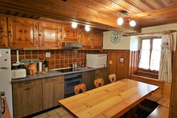 Una cocina de madera con una mesa y bancos de madera, una estufa, un fregadero y un reloj en la pared.