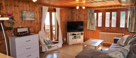 A wooden cabin interior with a sofa, TV, white dresser, and a dining table.