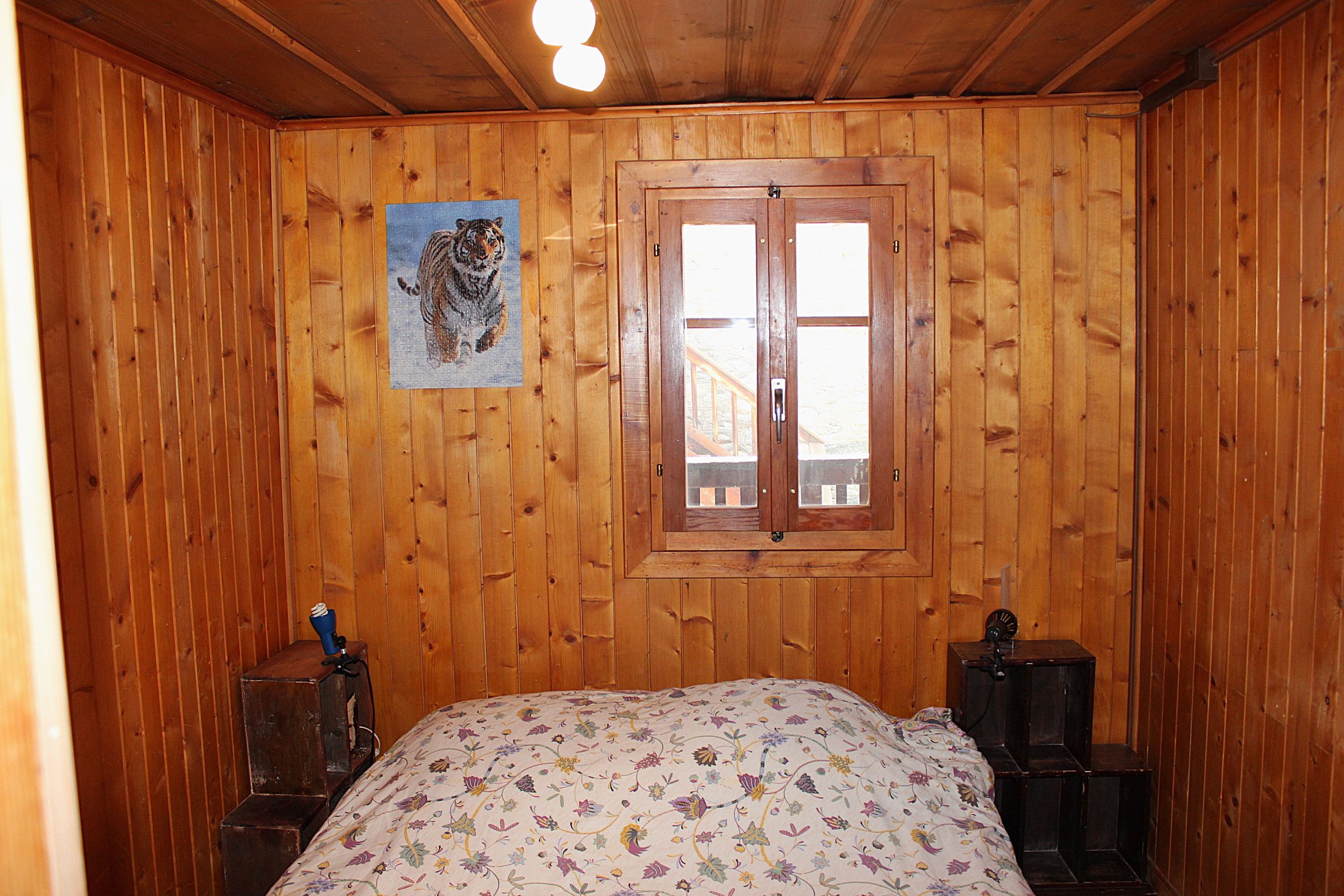 Ein Zimmer mit Holzwandverkleidung, einem Bett, einem Fenster mit Blick und einem Tigergemälde an der Wand.