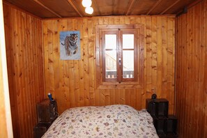 A wooden-paneled room with a bed, a window with a view, and a tiger painting on the wall. - le Tsenevirè (Evolène)