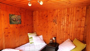 Una habitación pequeña y acogedora con paredes de madera, dos camas individuales con almohadas, una mesita de noche con lámpara y un adorno en la pared.