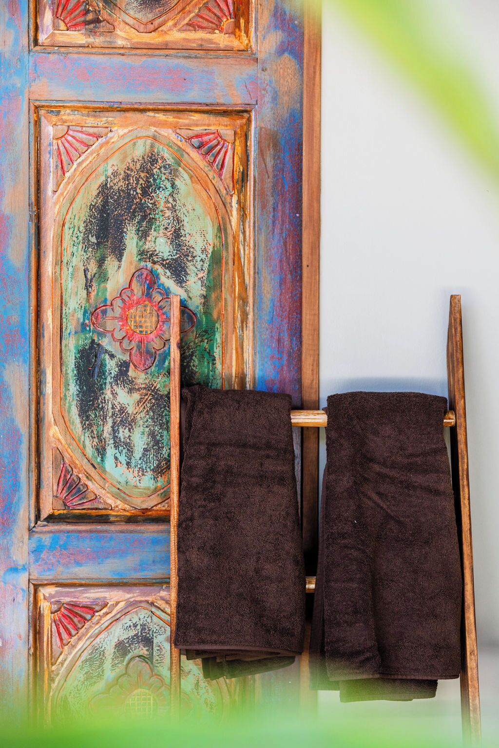 A bathroom with a wooden door featuring a colorful, distressed design. Two dark towels are hanging on a wooden towel rack.
