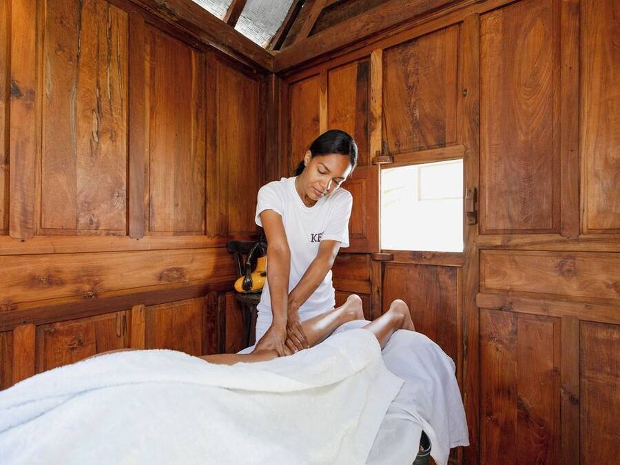 A wooden room with a massage table, a massage therapist, and a small table with a yellow object.