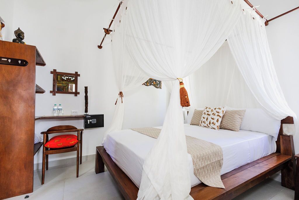 A room with a bed under a canopy, a wooden desk with a chair, and a small cabinet.