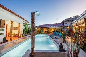 Un área de piscina con una estructura de madera, sillas de descanso y una estatua.