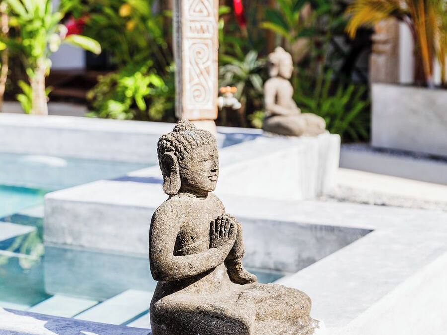 Une statue de Bouddha en pierre, située dans un espace piscine, avec un sol carrelé et un pilier décoratif.
