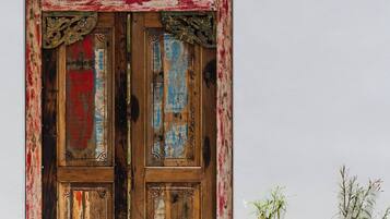 Una puerta de madera rústica con pintura colorida, un tejado de paja y una pared blanca con plantas en macetas.